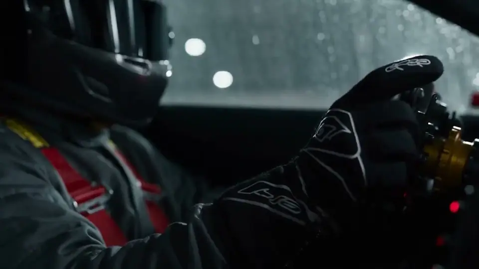 A driver's gloved hands on a wheel, rain on the windscreen.